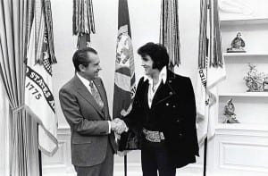 Two men shaking hands in front of flags.